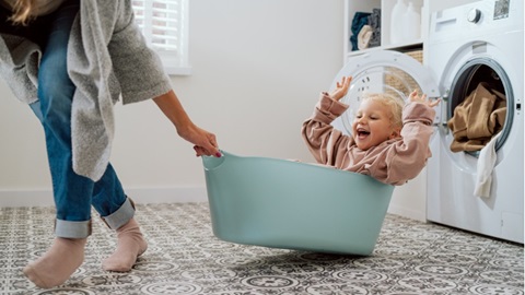 kind zit in wasmand en vrouw speelt met haar in het washok voor de wasmachine